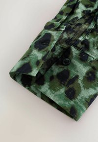 Groene luipaardprint shirtmanchet met zwarte accenten, gemaakt van stoffen met een zachte textuur. Voorzien van een knoop en een opgestikte naaddetail.