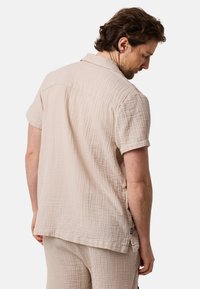 Camicia a maniche corte beige chiaro realizzata in tessuto texturizzato, con colletto e orlo dritto con spacchi laterali.