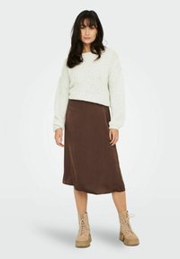Pull en tricot crème, jupe longue en satin marron, et bottes à plateforme en cuir tan avec lacets. Textures douces, coupe décontractée et style casual.