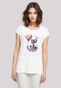 Weißes Baumwoll-T-Shirt mit einem grafischen Druck eines Skeletts, das einen herzförmigen Luftballon hält, verziert mit Schmetterlingen. Lässige, entspannte Passform.