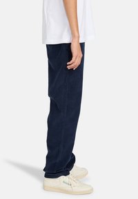 Pantalones de pana azul marino con un diseño de pierna recta, que cuentan con bolsillos laterales y se llevan con zapatillas blancas. Se aprecia la textura de la tela.