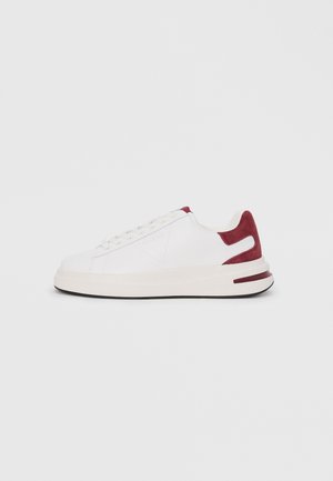 White sneaker with red suede accents, textured upper and rubber sole. Features flat laces and a logo on the side. Minimalist design.