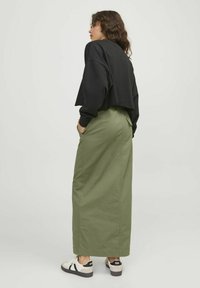 Sudadera negra corta con mangas largas, combinada con una falda verde oliva de cintura alta. Cuenta con bolsillos y un corte recto. Llevada con zapatillas.