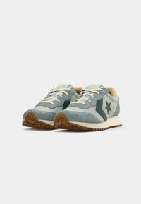 Light blue suede sneakers with green accents, white laces, and a rubber sole. Features logo star on the side and textured surface.