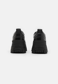 Zwarte sneakers met een bovenwerk van gestructureerd leer, een gevoerde kraag en dikke rubberen zolen met een onderscheidend profielpatroon en merkaanduiding.