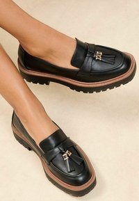 Mustad nahast loafers, millel on lame kummist tald. Omab dekoratiivset rippuvaid pomponeid ja kulla aktsente. Üksikasjalikult värvitud sileda viimistlusega.