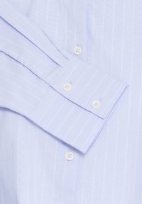 Chemise bleu clair à fines rayures blanches verticales, gros plan montrant le poignet avec deux boutons et une partie de la rangée de boutons à l'avant.
