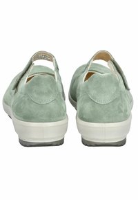 Zapatos de ante verde claro con puntera redonda y tira en la parte posterior, que presentan una suela de goma blanca y detalles de costura en el talón.