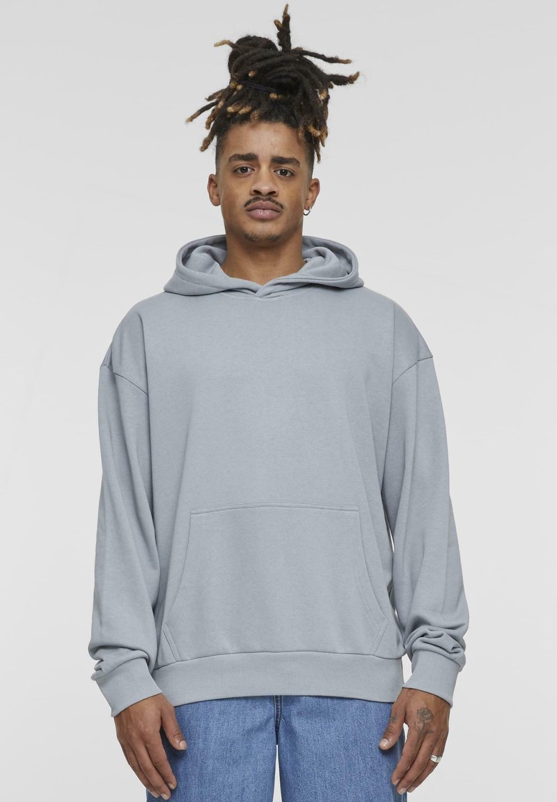 Light grey hoodie made of soft fabric; features a front pocket, drawstring hood, and ribbed cuffs. Worn with blue denim jeans.