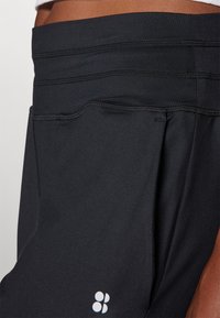 Black athletic shorts featuring a textured waistband and side pocket, with contrasting brown accents and a small white logo near the hem.