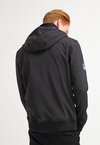 Svart hoodie med en mjuk textur, som har en dragsko huva, ribbade manschetter och en ficka på baksidan. Runt logotypdetalj på ärmen.