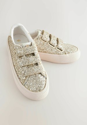 Mirdzoši zelta tenisi ar auduma augšdaļu, trim Velcro siksnām un baltu gumijas zoli ar teksturētām akcentiem.