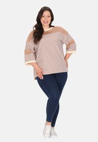 Hanorac rayat în bej și crem, cu mâneci 3/4, purtat cu blugi skinny bleu închis și adidași albi.