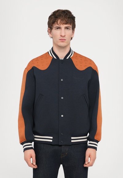 Tengerész navy varsity dzseki narancssárga bőr vállakkal és díszítő mintákkal, bordázott csíkozott mandzsettákkal és patentos záródással.