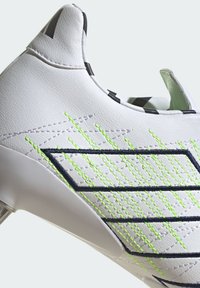 Zapatilla deportiva blanca con un diseño elegante, que cuenta con patrones de costura en verde y marino, una parte superior sintética lisa y una silueta de perfil bajo.