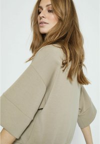 Světlý béžový, oversized top s širokými rukávy a hladkou texturou. Jednoduchý design s uvolněným střihem, bez viditelných vzorů nebo kovových prvků.