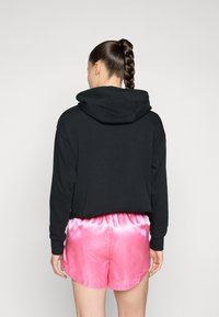 Hanorac scurt negru cu un glugă mare și mâneci lungi, asociat cu pantaloni scurți din satin roz strălucitor. Textură netedă cu un elastic la talie.