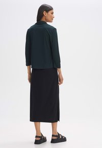 Black midi skirt paired with a dark green blouse, featuring a relaxed fit and a collar. The outfit is complemented by black sandals.
