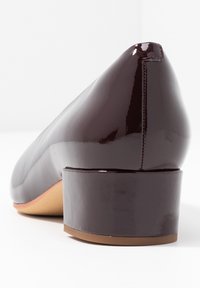 Talons en cuir verni bourgogne avec un bout rond et un talon carré. Fini lisse, détails cousus sur le côté.