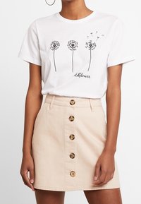 Hvid bomulds T-shirt med tre sorte dandelion illustrationer og ordet "wildflower." Sammen med en beige denim nederdel med knapper.