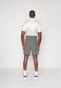 Gray shorts with a smooth texture and multiple pockets, paired with a light-colored polo shirt, viewed from the back.