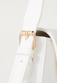 White faux leather bag strap with a gold-tone metal buckle detail, featuring a smooth texture and clean stitching. Close-up view.