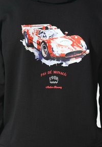 Sudadera negra con un gráfico multicolor de un coche de carreras vintage, con el texto "PAS DÉ MONACO 1988" y "Atelier Racing" en rojo.