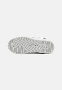 Suela de zapatilla blanca con patrón de agarre texturizado y logo de Reebok. Presenta un diseño de banda de rodadura en espiga con elementos de tracción hexagonales.