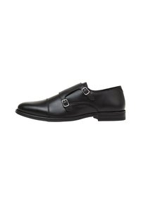 Chaussure en cuir noir avec double boucle, bout arrondi, texture lisse, semelle basse et design minimaliste.