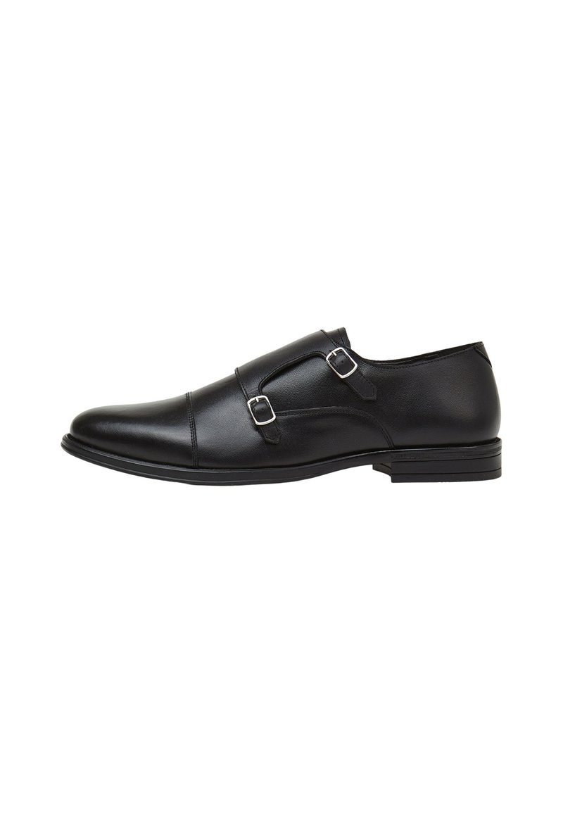 Chaussure en cuir noir avec double boucle, bout arrondi, texture lisse, semelle basse et design minimaliste.