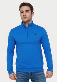 Blauwe pullover sweatshirt met hoge kraag, rits en geribde manchetten. Voorzien van een klein zwart logo op de borst. Zachte stof, aansluitend ontwerp.