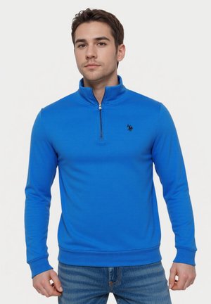 Pulover bleumarin cu guler înalt, fermoar și manșete strâmte. Prezintă un mic logo negru pe piept. Material moale, design ajustat.