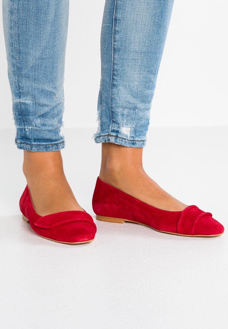 Rode suède ballerina's met een ronde neus, horizontale plooidetails en een platte zool. Draag ze met versleten lichtblauwe jeans.