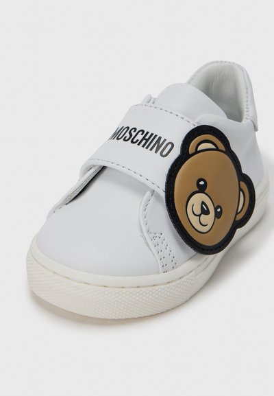 Λευκό δερμάτινο αθλητικό παπούτσι με ιμάντα Velcro, διακοσμημένο με επιφάνεια προσώπου μαύρης αρκούδας και το λογότυπο "Moschino" στον ιμάντα. Με υφή σόλα από καουτσούκ.