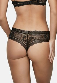 Culotte en dentelle noire avec des motifs floraux, des bords festonnés et un accent doré au dos. Matériau doux et transparent avec une texture délicate.