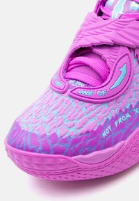 Κοντινό πλάνο ενός παπουτσιού αθλητικού με μοτίβο σε μοβ και μπλε χρώμα, με υφή στη σόλα, χοντρές κορδόνια και πλαστικό λουρί που φέρει μερικό κείμενο και γραφικά στοιχεία.