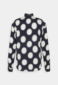 Chemise à manches longues en tissu bleu marine foncé avec de gros pois blancs, col classique, et poignets boutonnés. Texture lisse.