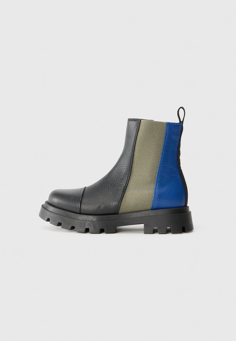 Botas Chelsea con punta de cuero negro, paneles laterales grises y acentos en azul y oliva. Suela de goma gruesa con un patrón de tracción para agarre.