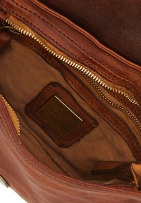 Interno di una borsa a tracolla in pelle marrone che mostra una zip dorata, un rivestimento in tessuto e un'etichetta del marchio. Presenta una texture liscia e un design pratico.