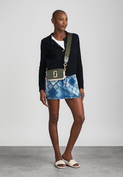 Green handbag with gold hardware, worn crossbody. Black ribbed sweater, denim mini skirt with diamond pattern, and white slide sandals.