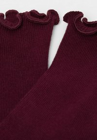 Burgundowa ryfrowana tkanina z falistym, falbaniastym wykończeniem. Materiał wydaje się miękki o teksturowanej powierzchni, ukazującej wyraźne prążki.