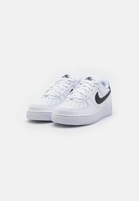 Biele kožené tenisky s perforáciami na špičke, čierny Nike swoosh, ploché šnúrky a gumová podrážka s drsným povrchom.