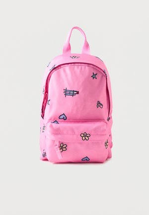 Pink rygsæk med små sorte, lilla og gule kruseduller af blomster, hjerter, stjerner og musikalske noder på en ensfarvet baggrund.