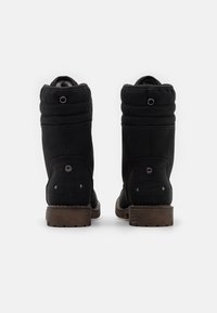 Bottes isolées noires avec un bout arrondi, une doublure en peluche, un dessus matelassé, un détail de logo et des semelles en caoutchouc marron robustes.