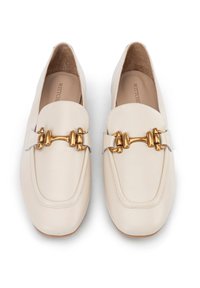 Mocassini in pelle beige con hardware in tonalità oro, caratterizzati da una barra decorativa sulla parte anteriore e una punta arrotondata. Texture liscia e cuciture minime.
