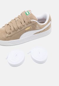 Baskets en daim beige avec accents blancs et semelle texturée. Comprend deux lacets blancs. Détail du logo doré sur le côté.