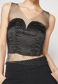 Czarny satynowy top o dopasowanym kroju, z siateczkową nakładką i srebrnymi ozdobami z koralików przy dekolcie i na dole.