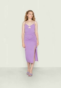 Vestido ajustado em lavanda com alças finas, recorte em forma de buraco na parte frontal, detalhe franzido na cintura e uma fenda até à coxa. Combinado com sandálias a condizer.