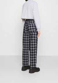Sudadera gris recortada de manga larga, combinada con pantalones de pierna ancha de cuadros en blanco y negro, que presentan bolsillos de parche y una cintura alta.