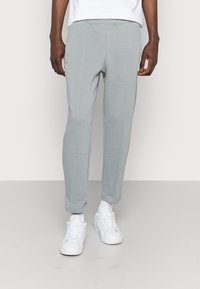 Ljusgrå sweatpants med elastiska muddar, sidofickor och subtila sömdetaljer, i kombination med vita sneakers. Mjuk tygtextur.